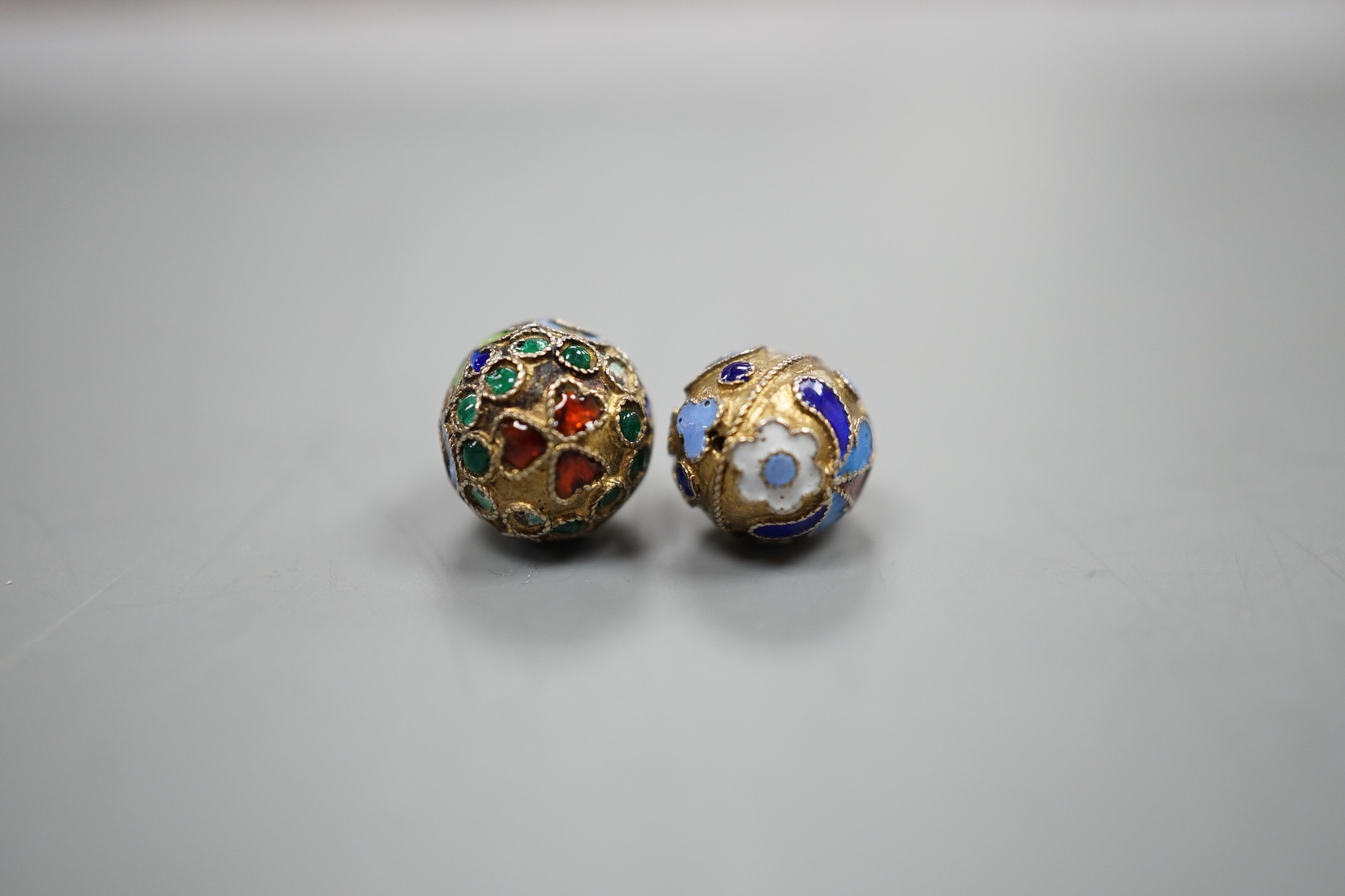 An early 20th century Russian 84 zolotnik and polychrome cloisonné enamel set egg pendant, maker's mark HT?, 17mm and a similar smaller egg pendant, maker's mark HM?.
